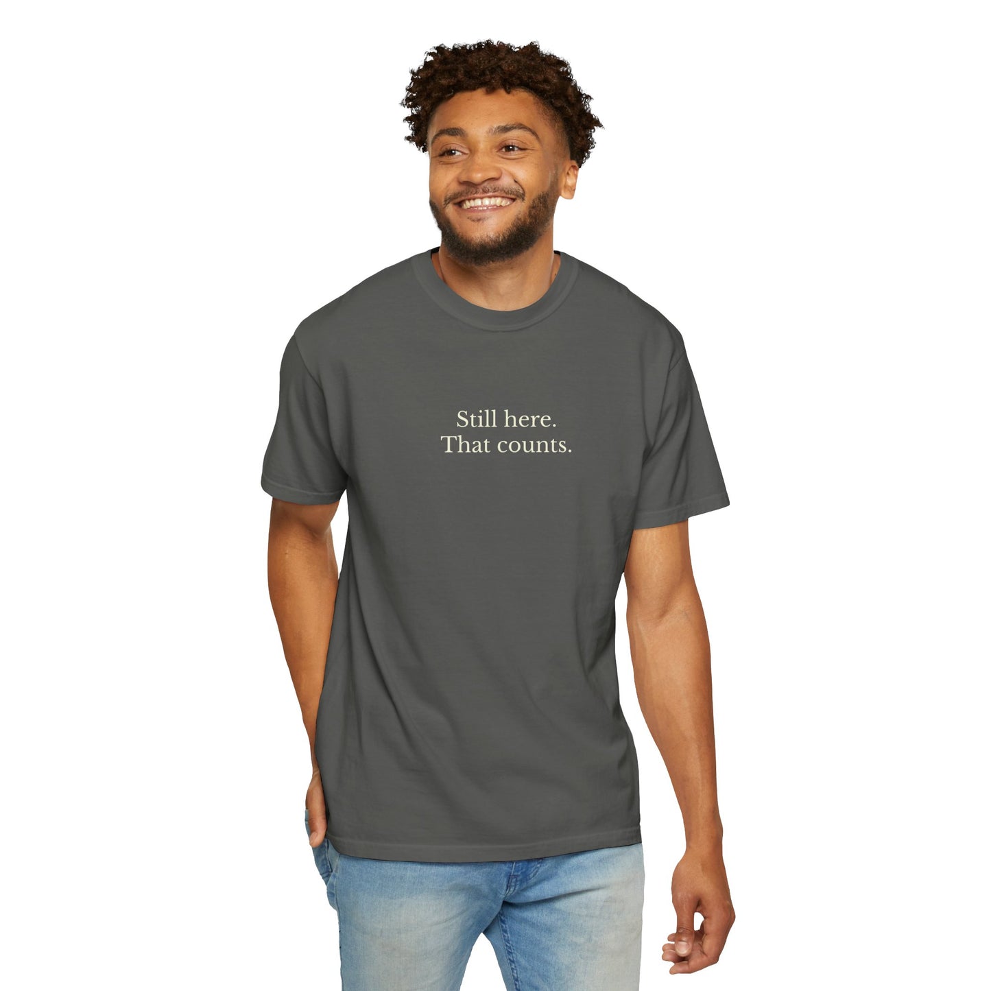 Man wearing a gray t-shirt with text 'Still here. That counts.' on a white background
