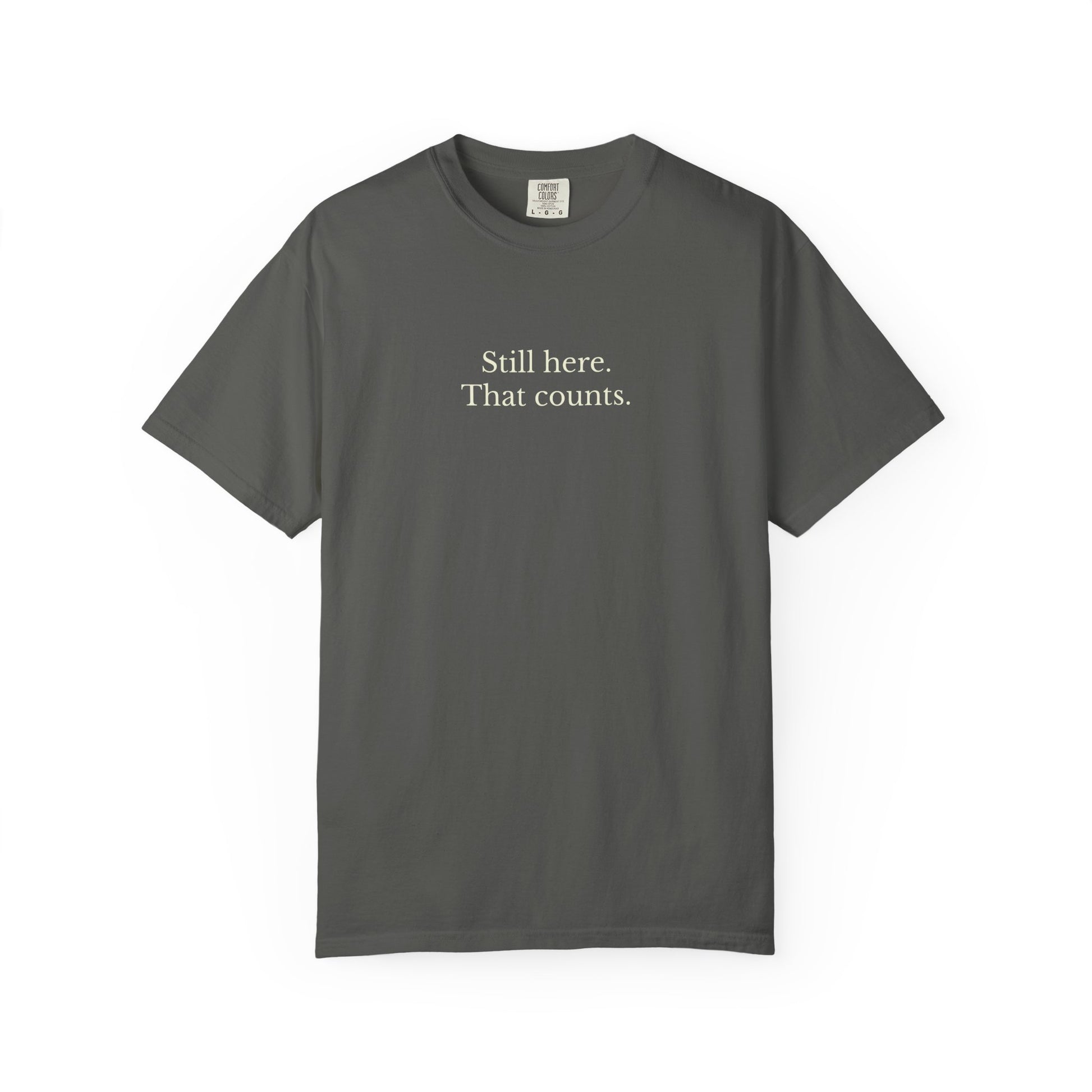 Gray t-shirt with text 'Still here. That counts.' on a white background