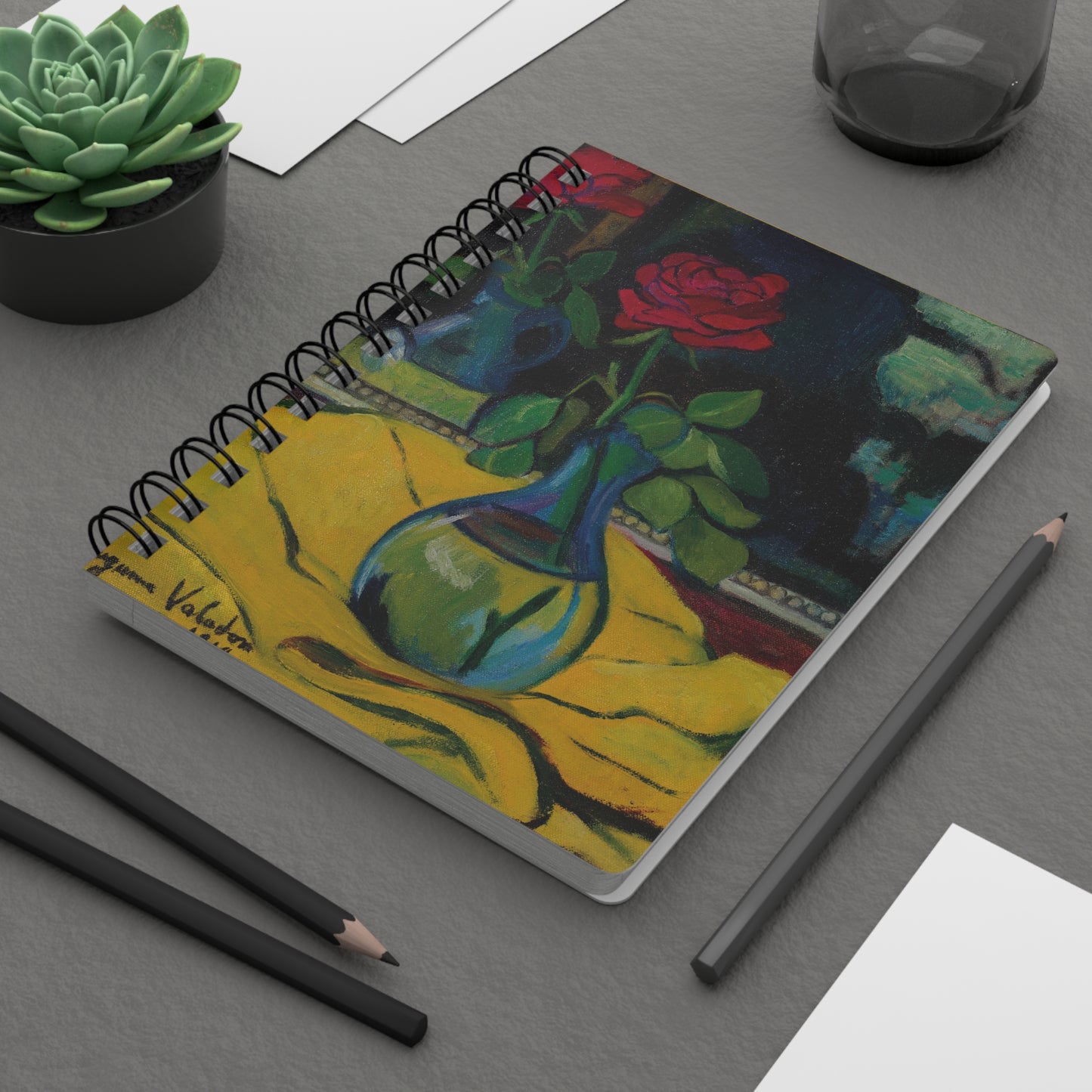 Notebook with artistic cover design on a gray surface with pencils and a plant.