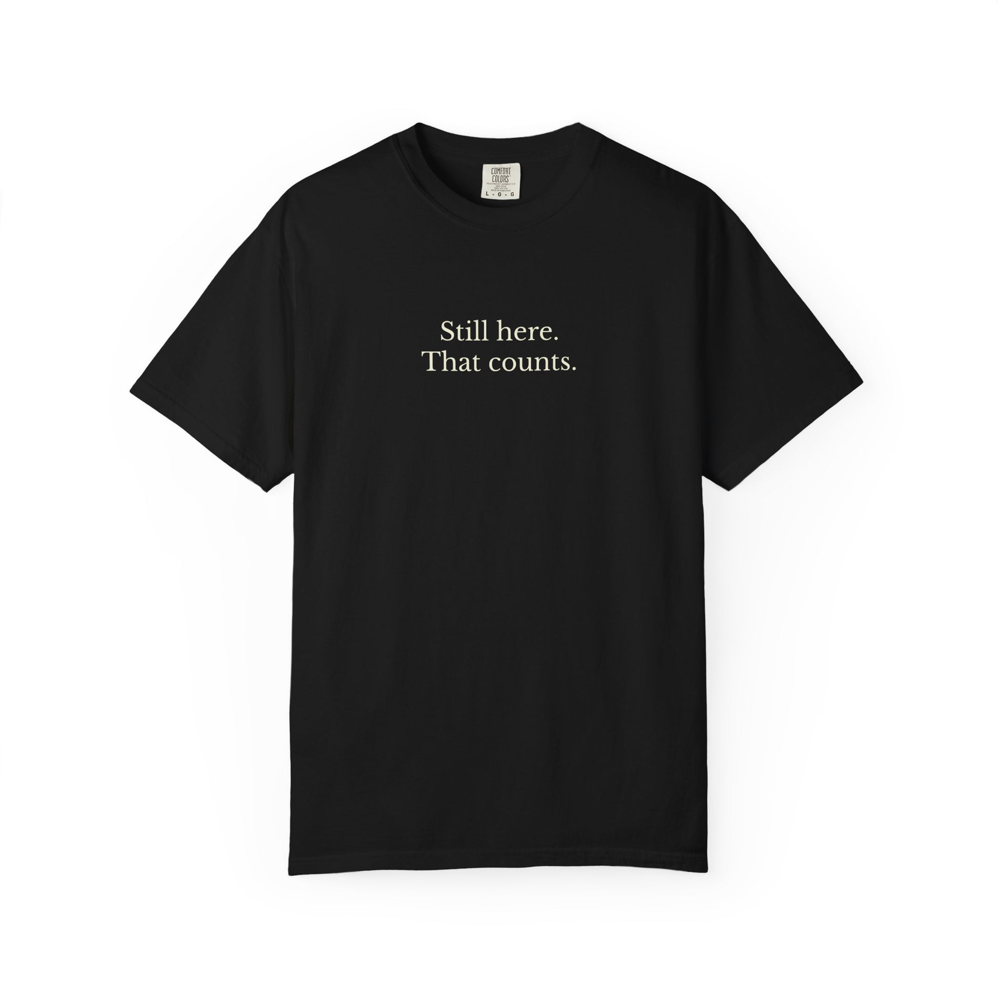 Black t-shirt with text 'Still here. That counts.' on a white background
