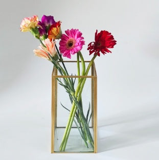 Glass vase with gold frame holding colorful flowers on a white background