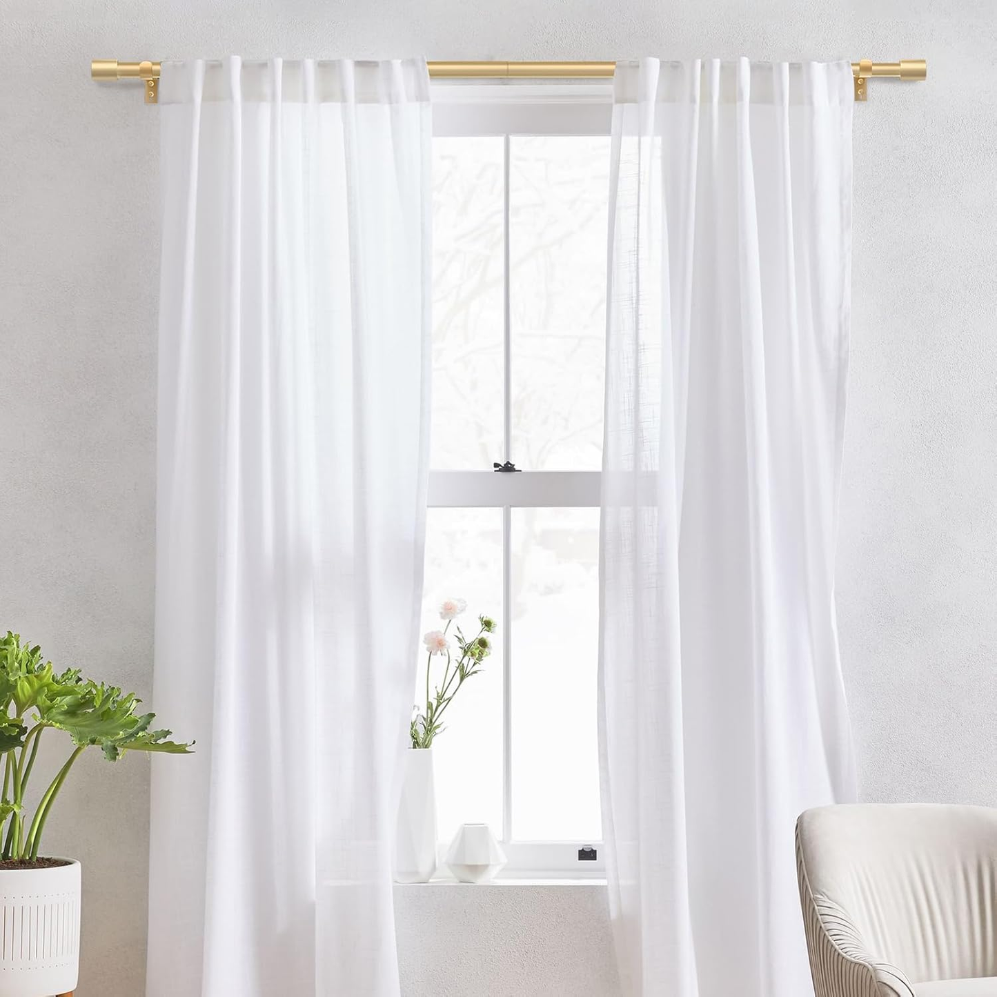 White curtains with gold curtain rods in a room with a plant and chair.