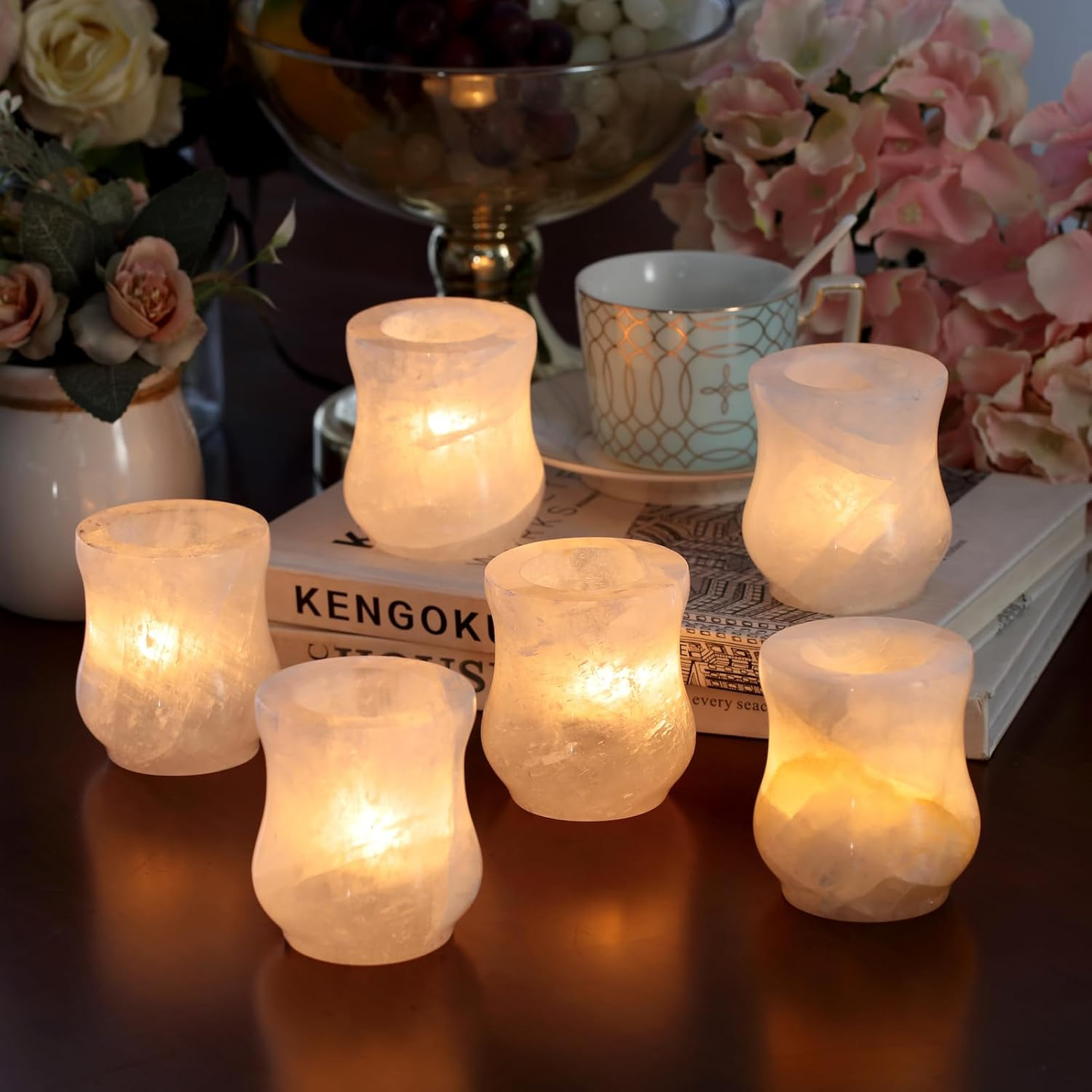 Set of six lit candle holders on a table with decorative items in the background